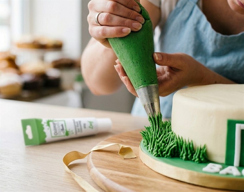close up photo of a cake decorator piping green buttercream grass around a football birthday cake