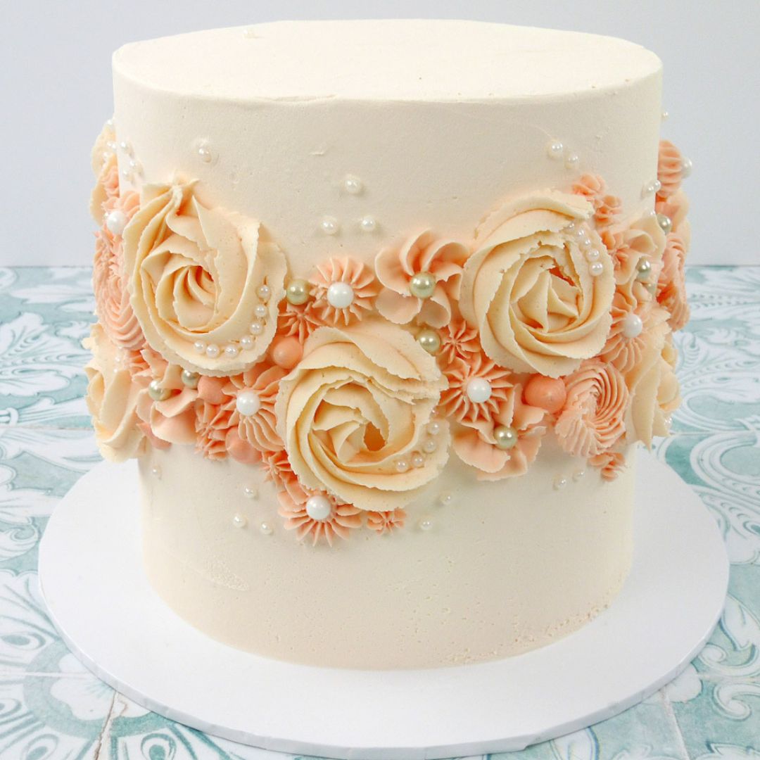 Buttercream celebration cake decorated with peach and coral swirls, edible pearl sprinkles, and piped rosettes